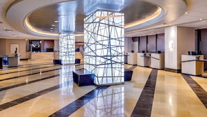 A modern hotel lobby with a central geometric column, reception desks, and a polished marble floor. - Courtland Grand Hotel, Trademark Collection by Wyndham (Atlanta)