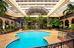 Une piscine intérieure dotée d’un toit en verre, entourée de chaises longues et de verdure.