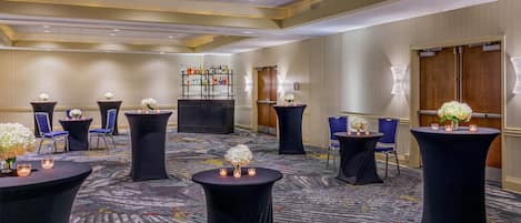 A hotel lobby with round tables, chairs, a bar area, and a floral display.