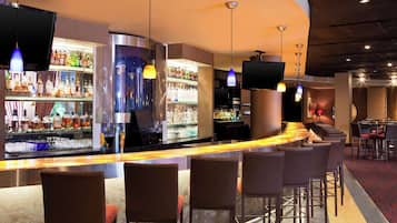 A bar area with multiple seating options, a well-stocked liquor shelf, and ambient lighting.