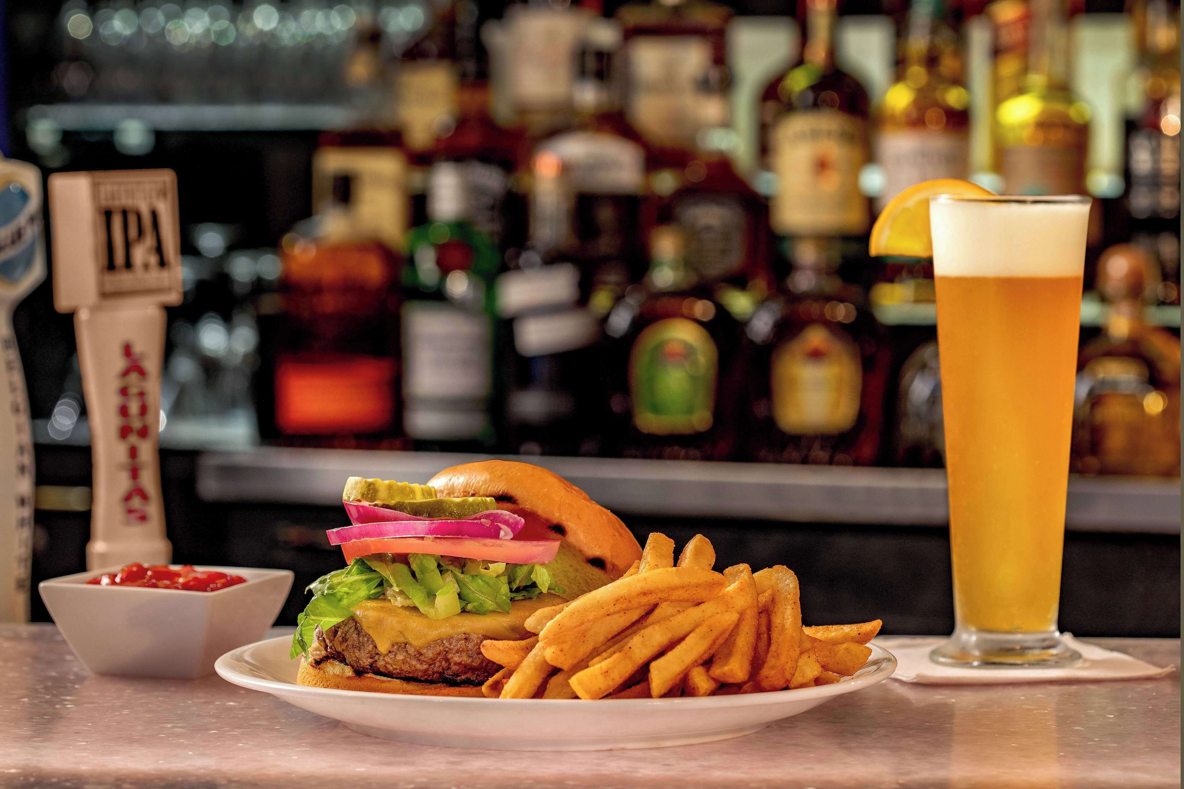 A burger with fries and a beer on a table with a bar in the background.