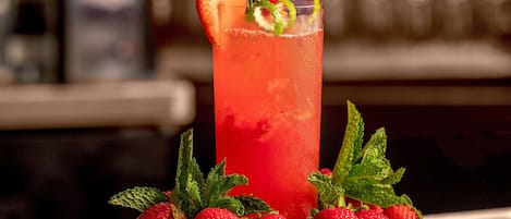 A tall glass of red beverage garnished with a strawberry and mint leaves, surrounded by fresh strawberries on a wooden surface.