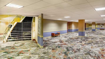 A spacious hotel lobby with a central staircase, a patterned carpet, and a seating area.