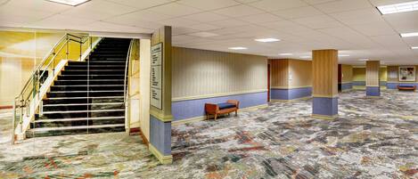 Un hall d’hôtel spacieux, doté d’un escalier central, d’une moquette à motifs et d’un espace salon.