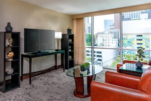 Habitación de hotel moderna con una televisión grande, una mesa de centro de cristal, sillones de cuero y vistas a la ciudad.