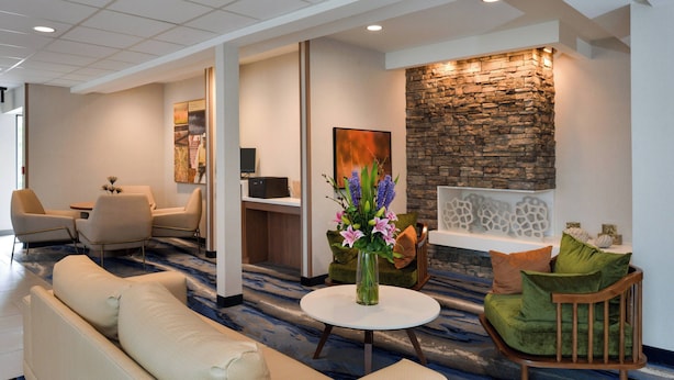 A modern lobby with a stone accent wall, a round white table with a vase of flowers, and a seating area with sofas and chairs. - Fairfield Inn & Suites by Marriott Arlington Six Flags (Arlington)