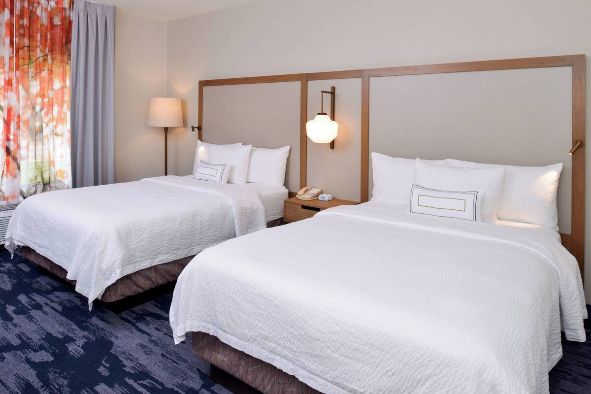 A hotel room with two beds, a nightstand with a lamp, and a telephone.