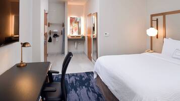 Habitación de hotel con cama, escritorio, silla y baño visible a través de una puerta abierta.