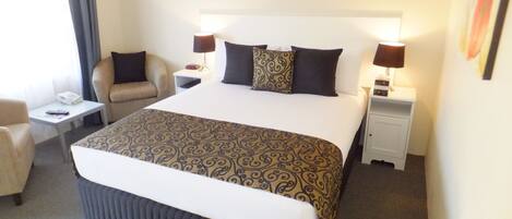 Een hotelkamer met een groot bed, twee nachtkastjes, een stoel en kunstwerken aan de muur.