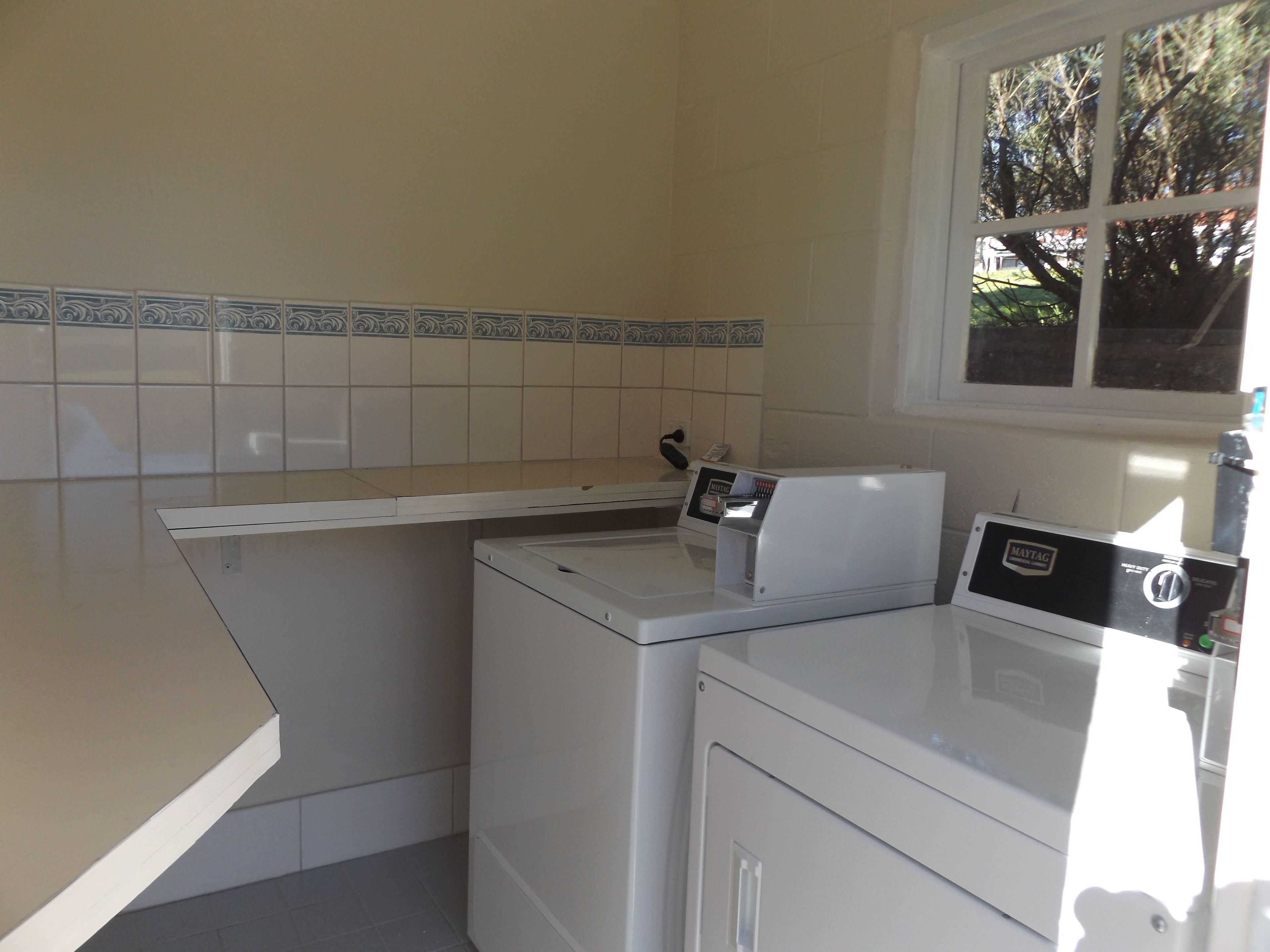 A laundry area with a washing machine and dryer, a countertop, and a window with a view of trees.