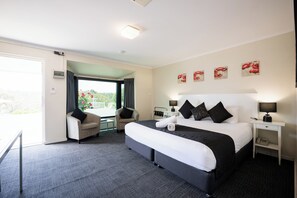 Relax in this serene space with a large bed, a bedside table, and a comfortable chair, offering a peaceful view of the surrounding greenery.