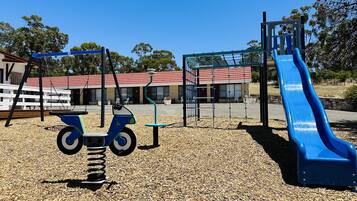 A playground with a blue slide and swings, surrounded by a gravel area.