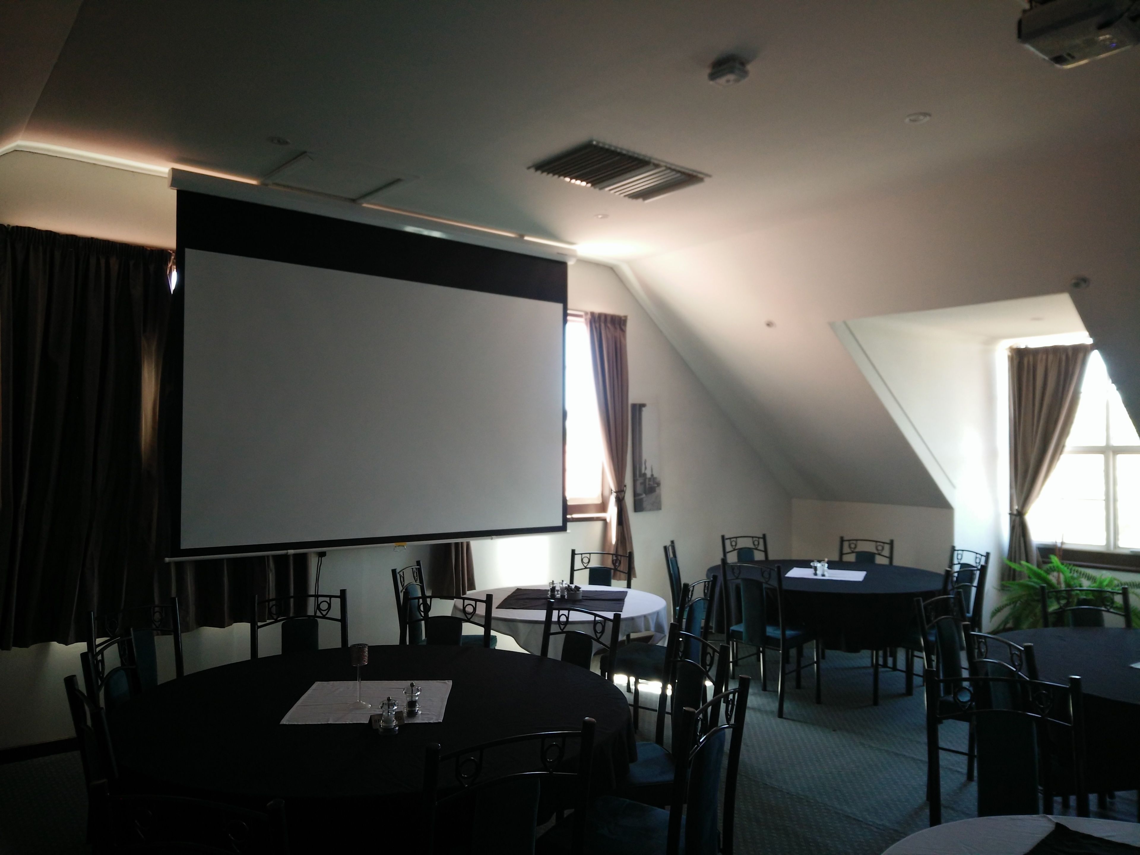 A conference room with a large screen, multiple tables, and chairs.