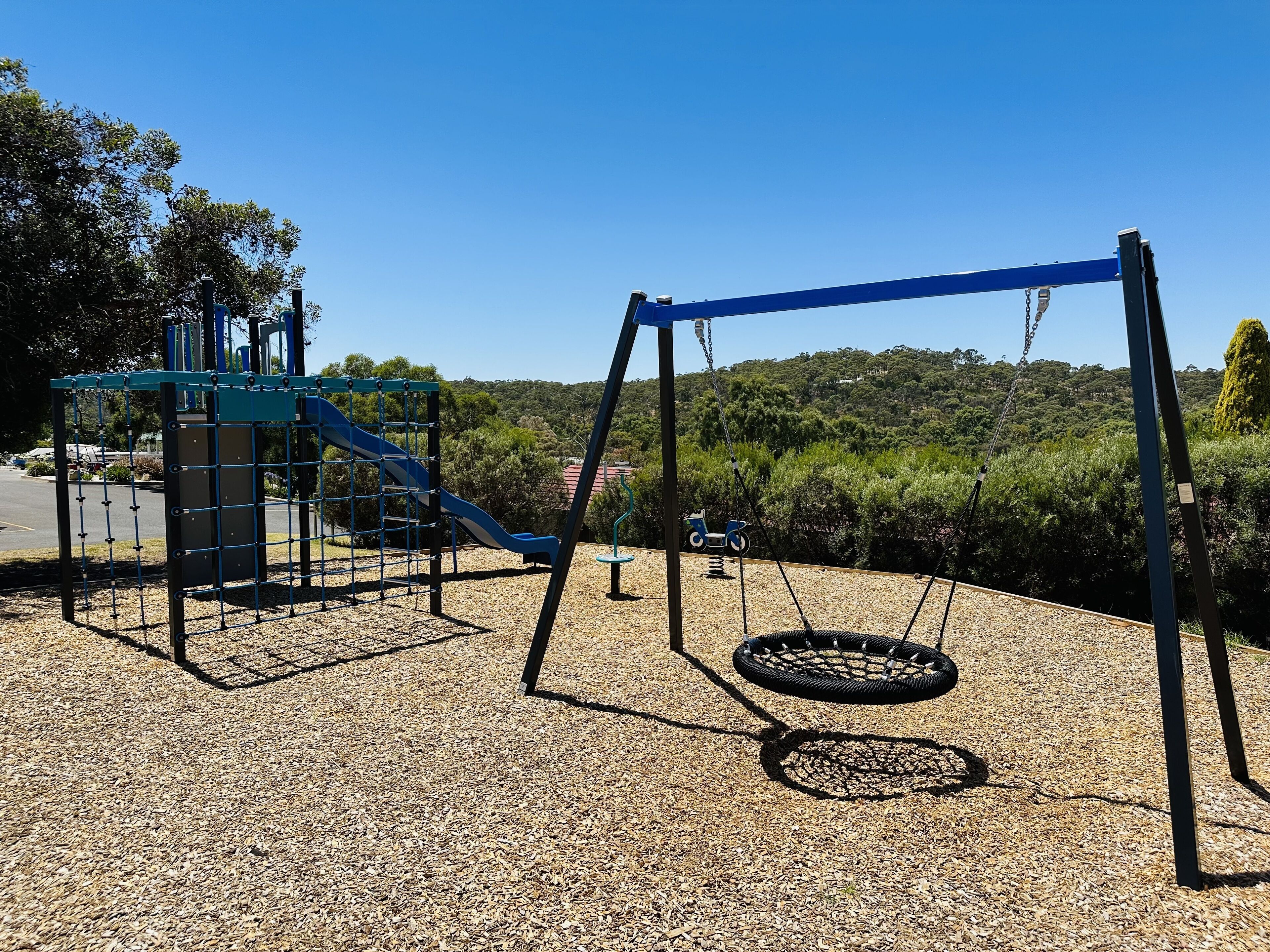 Un parque infantil con tobogán, columpios y un neumático colgante sobre suelo de grava.