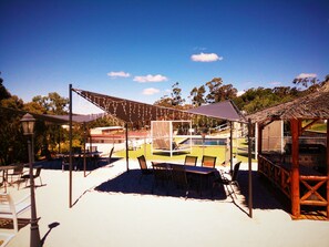 Relax in a covered patio area with tables and chairs, overlooking a pool and barbecue grill.
