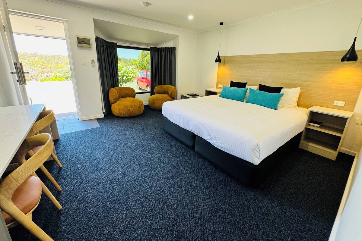 A hotel room with a bed, two armchairs, a desk, and a view of the outdoors.