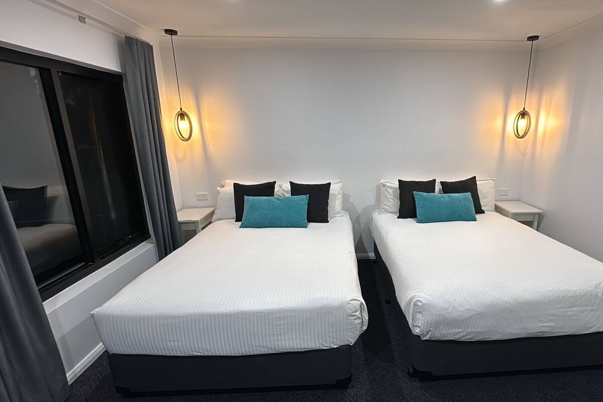 A hotel room with two single beds, each with a pillow and a bedside table.