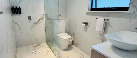 A modern bathroom with a glass-enclosed shower, a toilet, a sink with a large basin, and a window above the sink.