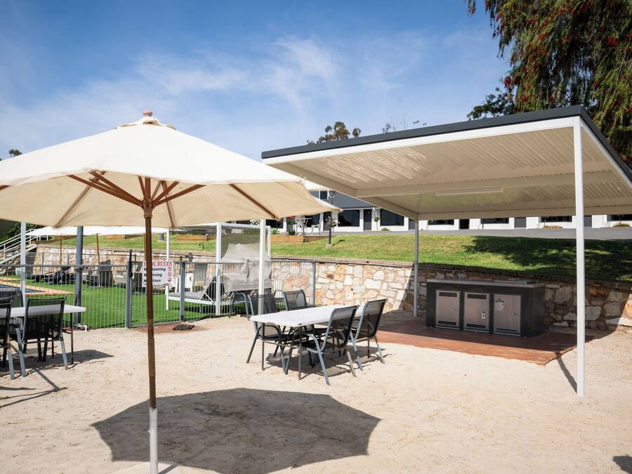 Un patio exterior con zona de estar cubierta, estación de parilla y vista a un campo deportivo.