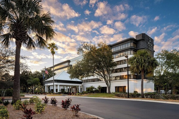 A modern hotel with a prominent 'Delta' sign, featuring a two-story structure with a glass facade, surrounded by landscaped gardens and palm trees. - Delta Hotels by Marriott™ Jacksonville Deerwood (Jacksonville)