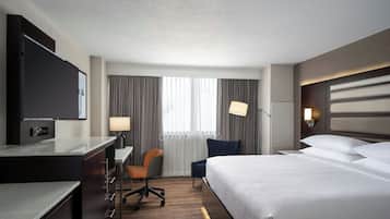 A hotel room with a bed, desk, chair, TV, and a window with curtains.