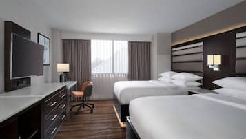 A hotel room with two beds, a desk with a chair, a TV, and a window with curtains.