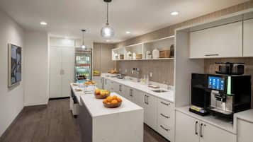 Una cocina moderna con armarios blancos, una isla central con fruta, una cafetera y un refrigerador empotrado.