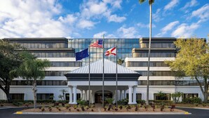 Un hotel moderno con fachada de vidrio, una entrada central con área cubierta y banderas de los Estados Unidos y del estado de Delaware.