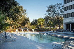 A swimming pool with lounge chairs and a patio area, surrounded by trees and a building. - Delta Hotels by Marriott™ Jacksonville Deerwood (Jacksonville)
