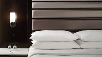 Una cama bien hecha con ropa blanca y una lámpara fijada en la pared.