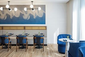 A modern restaurant with blue upholstered chairs, a round table, and a large abstract painting on the wall. - Delta Hotels by Marriott™ Jacksonville Deerwood (Jacksonville)