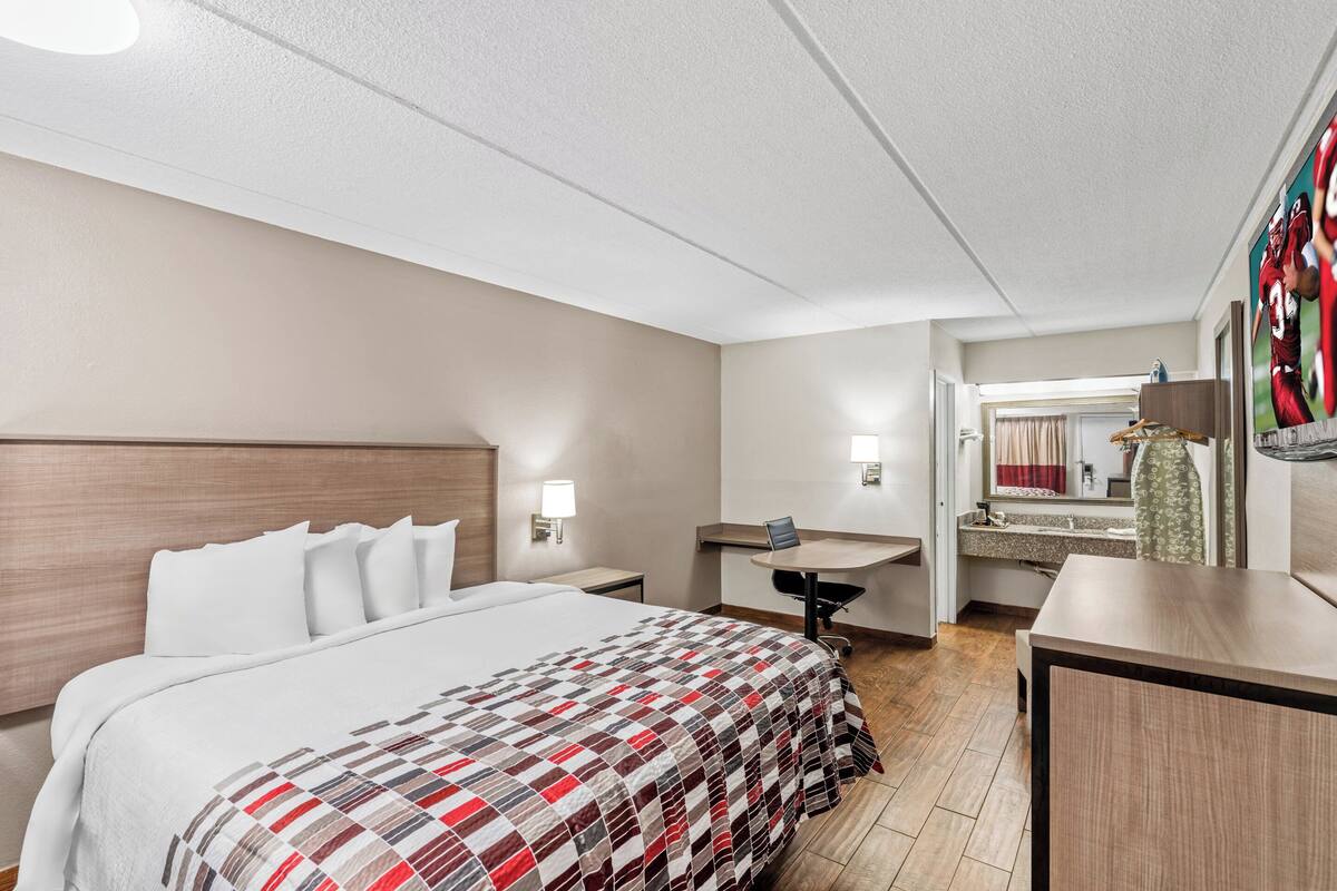 A hotel room with a large bed, a desk, a chair, and a mirror.