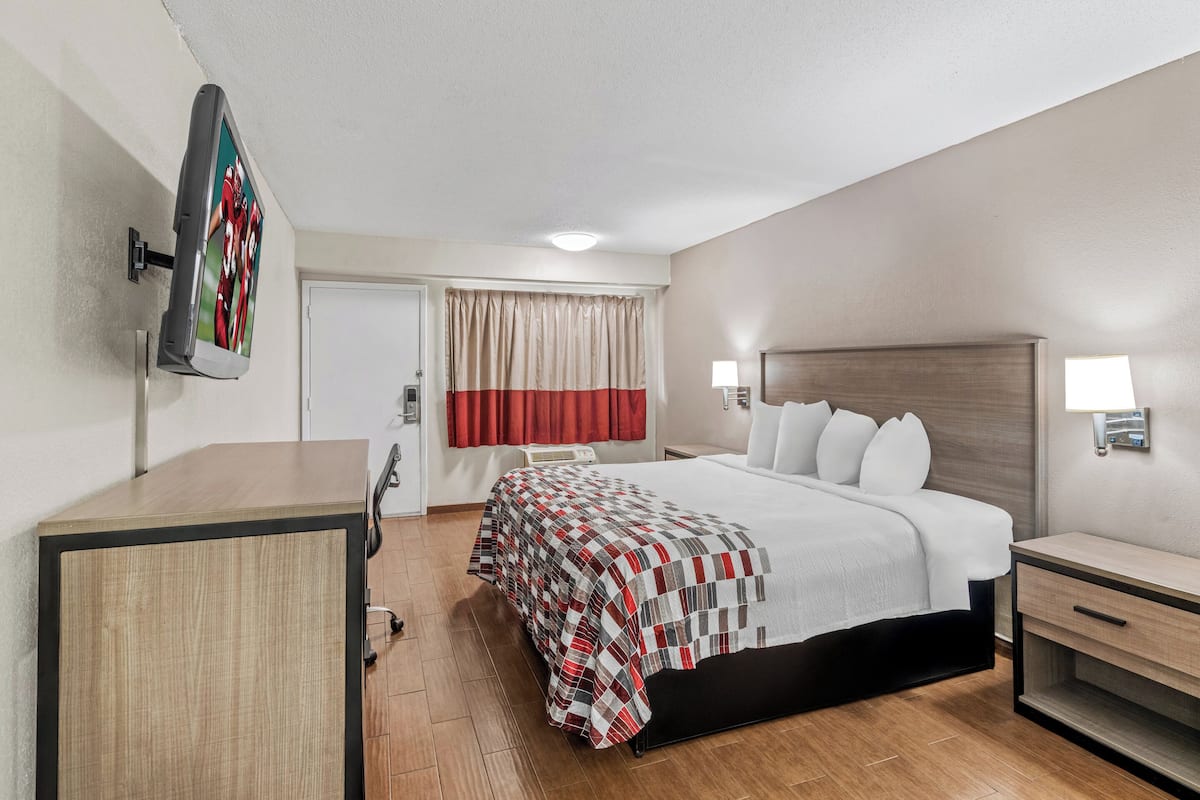A hotel room with a bed, bedside tables, a desk, a TV mounted on the wall, and a window with curtains.