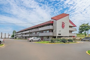 Un hotel Red Roof Inn con un edificio de dos pisos, estacionamiento y una zona ajardinada con flores.