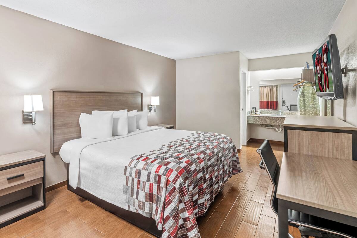 A hotel room with a large bed, bedside tables, a desk, and a TV.