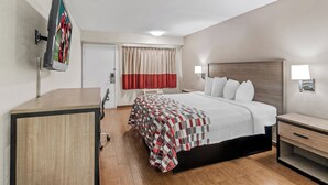 A hotel room with a bed, bedside tables, a desk, a TV mounted on the wall, and a window with curtains. - Red Roof Inn Jackson Downtown - Fairgrounds (Jackson)
