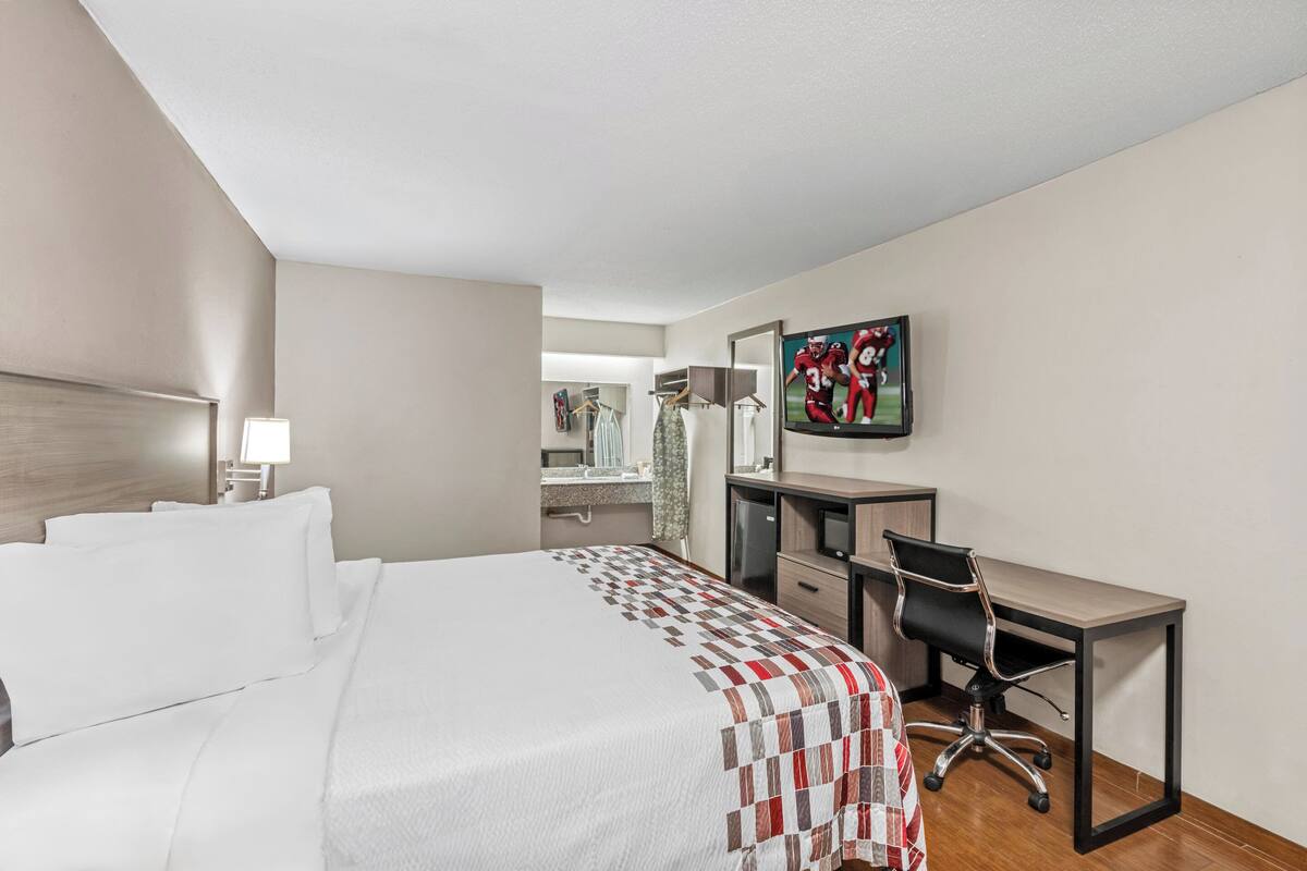 A hotel room with a large bed, a desk, a chair, a TV, and a mirror.