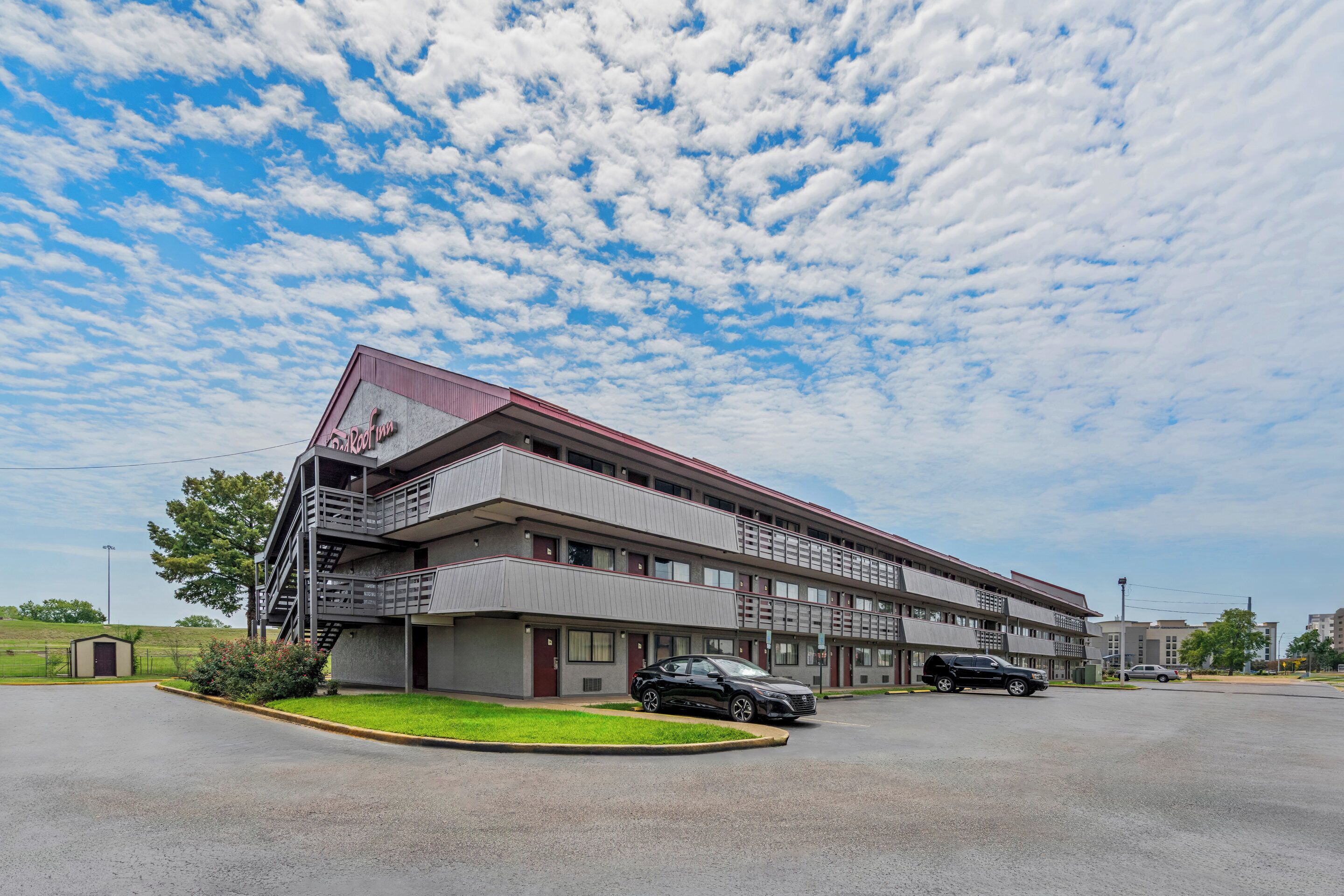 A motel with a red roof and multiple floors, featuring a parking lot with several cars.