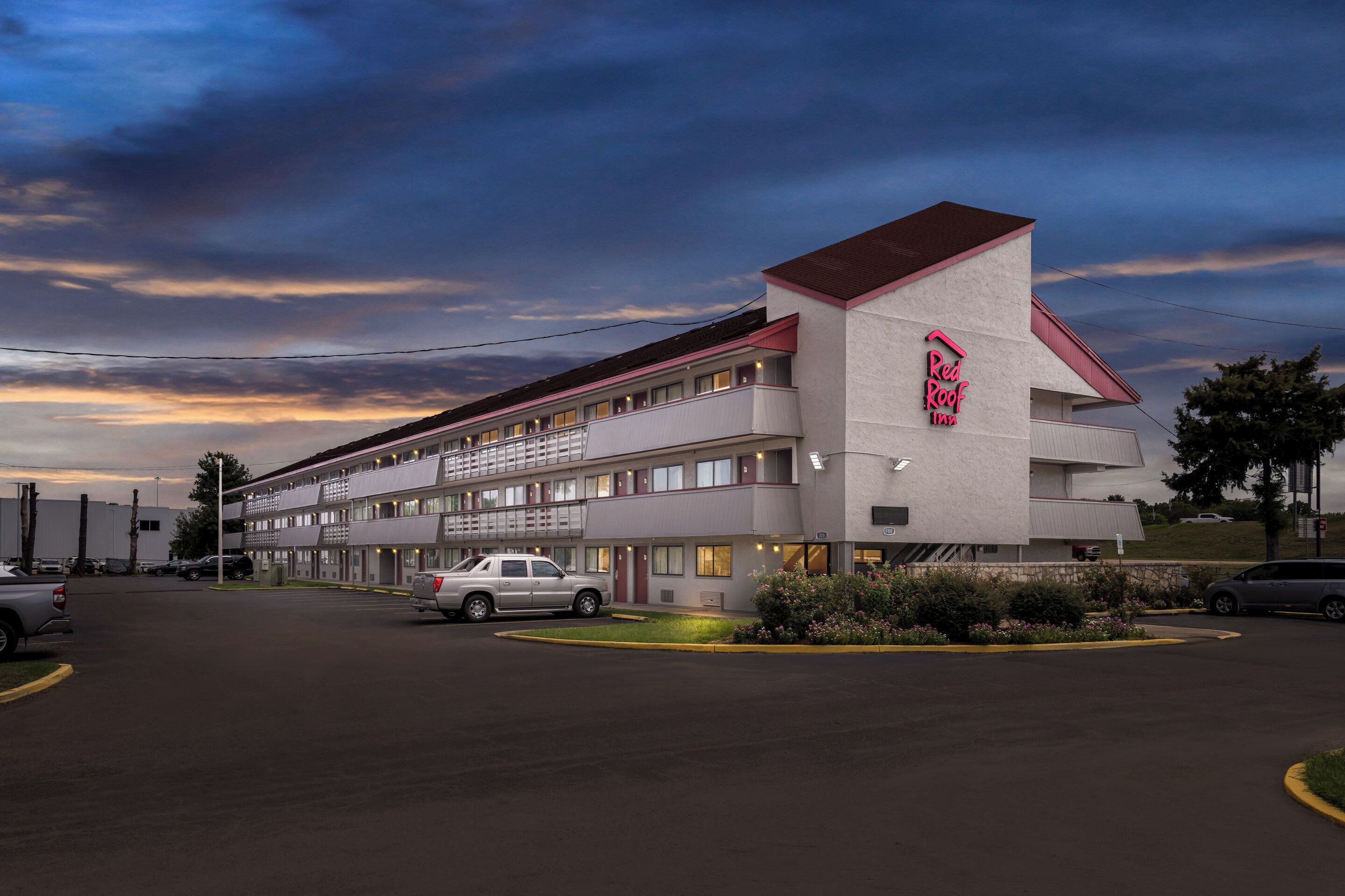 Um Red Roof Inn com estrutura de dois andares, estacionamento e área de jardim ajardinada.