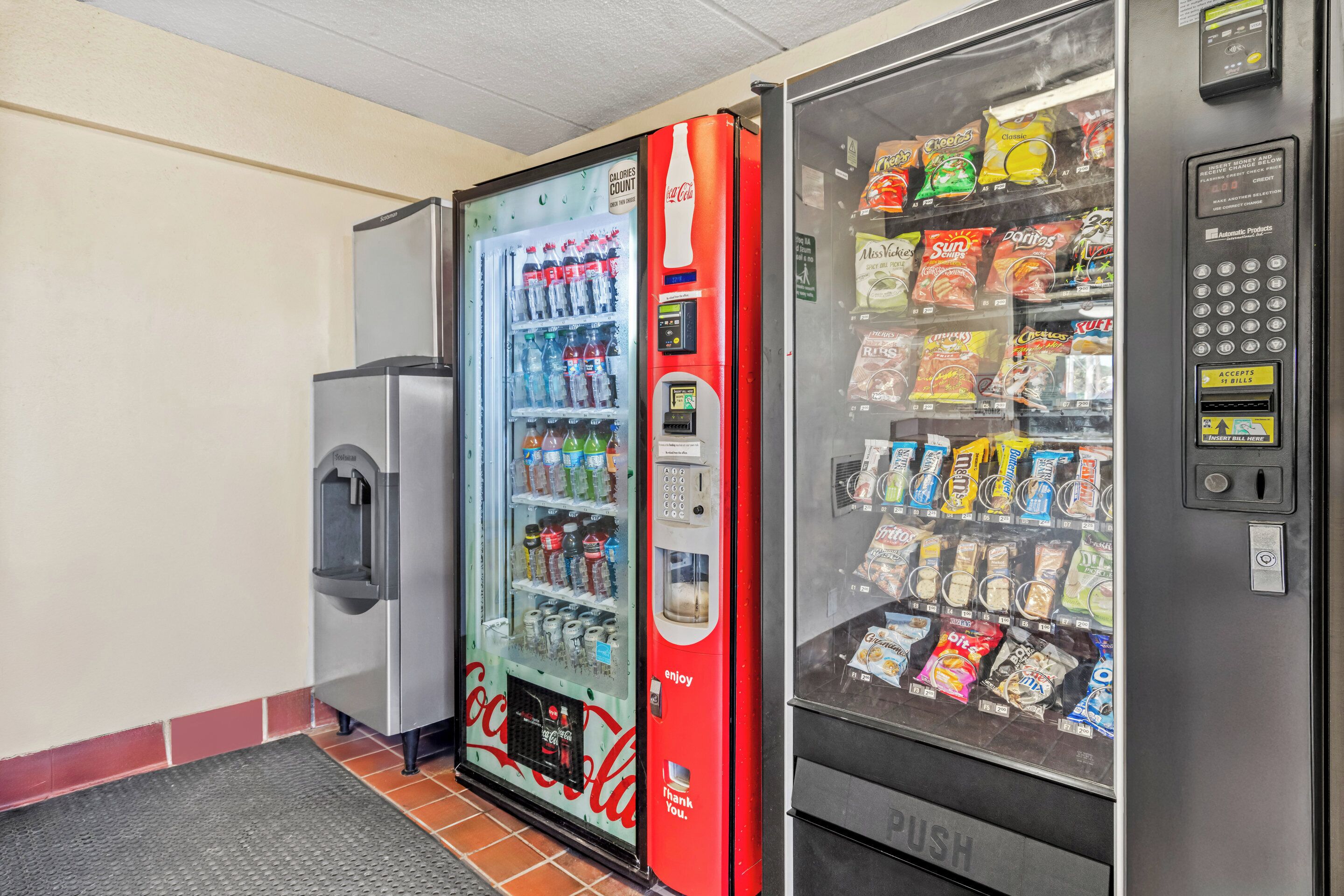 Uma área com máquinas de venda automática, incluindo uma máquina da marca Coca-Cola e uma máquina de venda por botão.