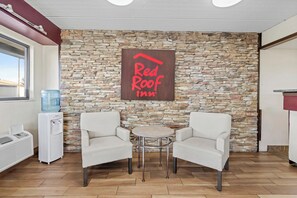 A Red Roof Inn room with a stone wall, two white armchairs, a small round table, a water cooler, and a window. - Red Roof Inn Jackson Downtown - Fairgrounds (Jackson)