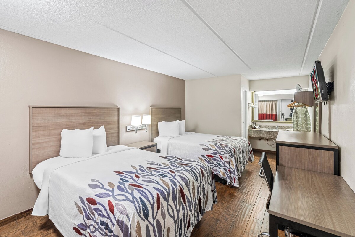 A hotel room with two beds, a desk, a mirror, and a TV.
