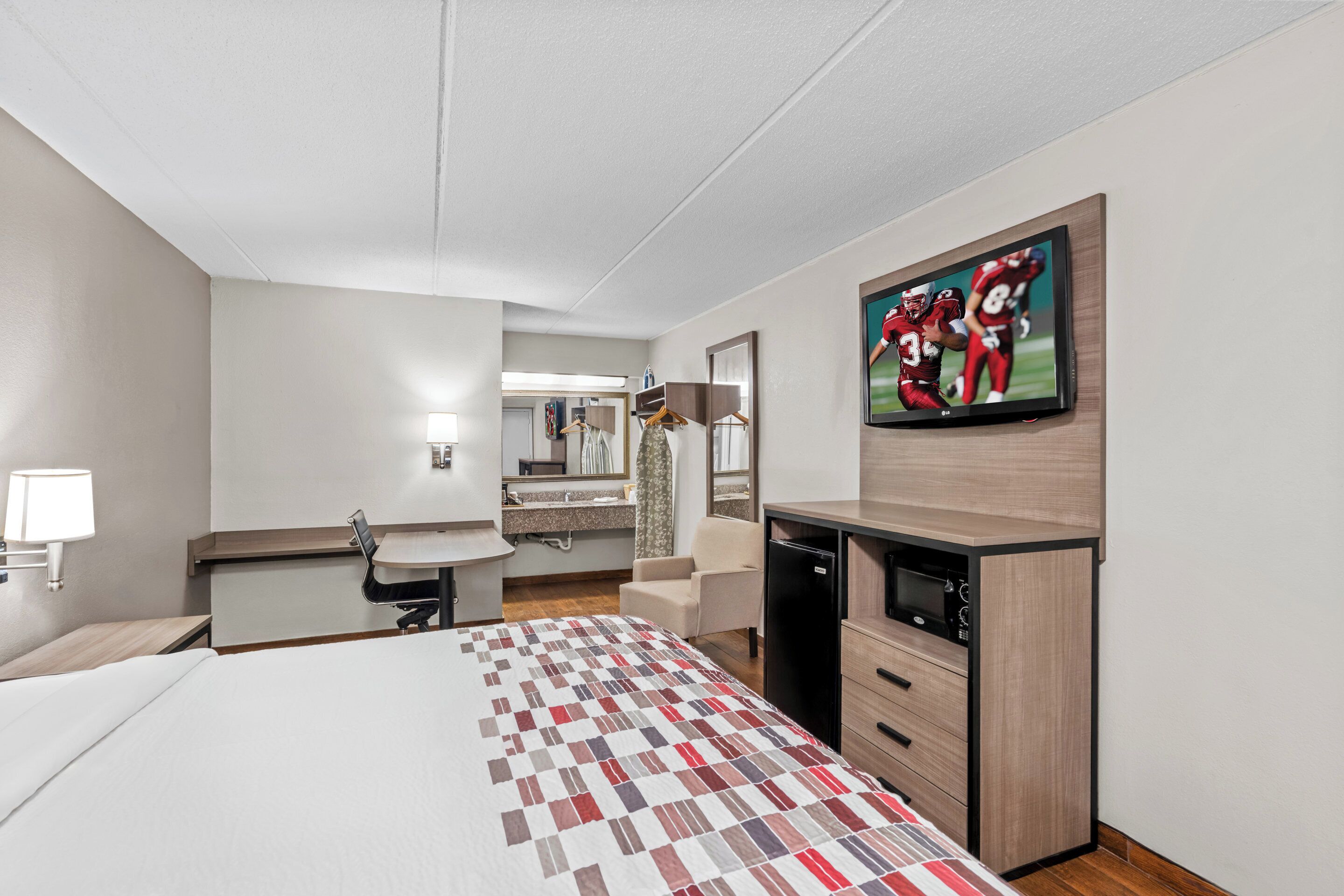 A hotel room with a bed, a desk, a chair, a TV, and a mirror.
