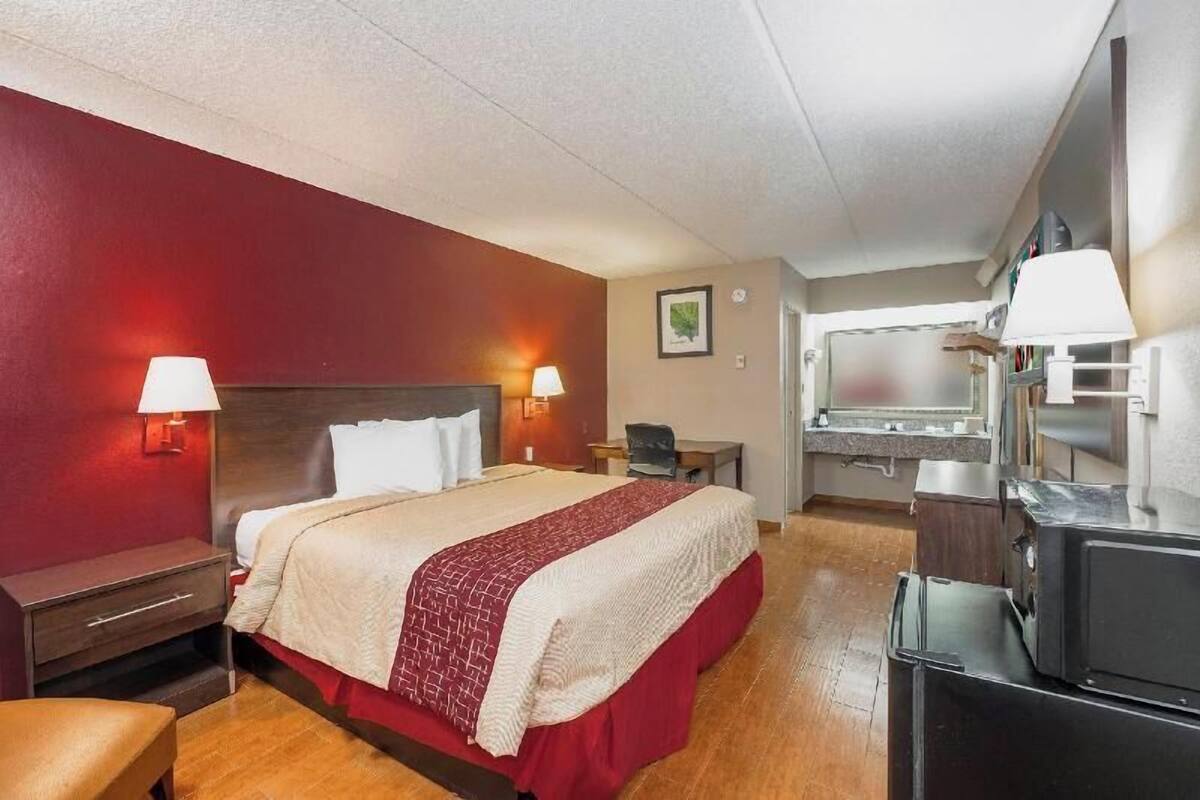 A hotel room with a bed, bedside tables, a desk, a chair, a TV, and a kitchenette.