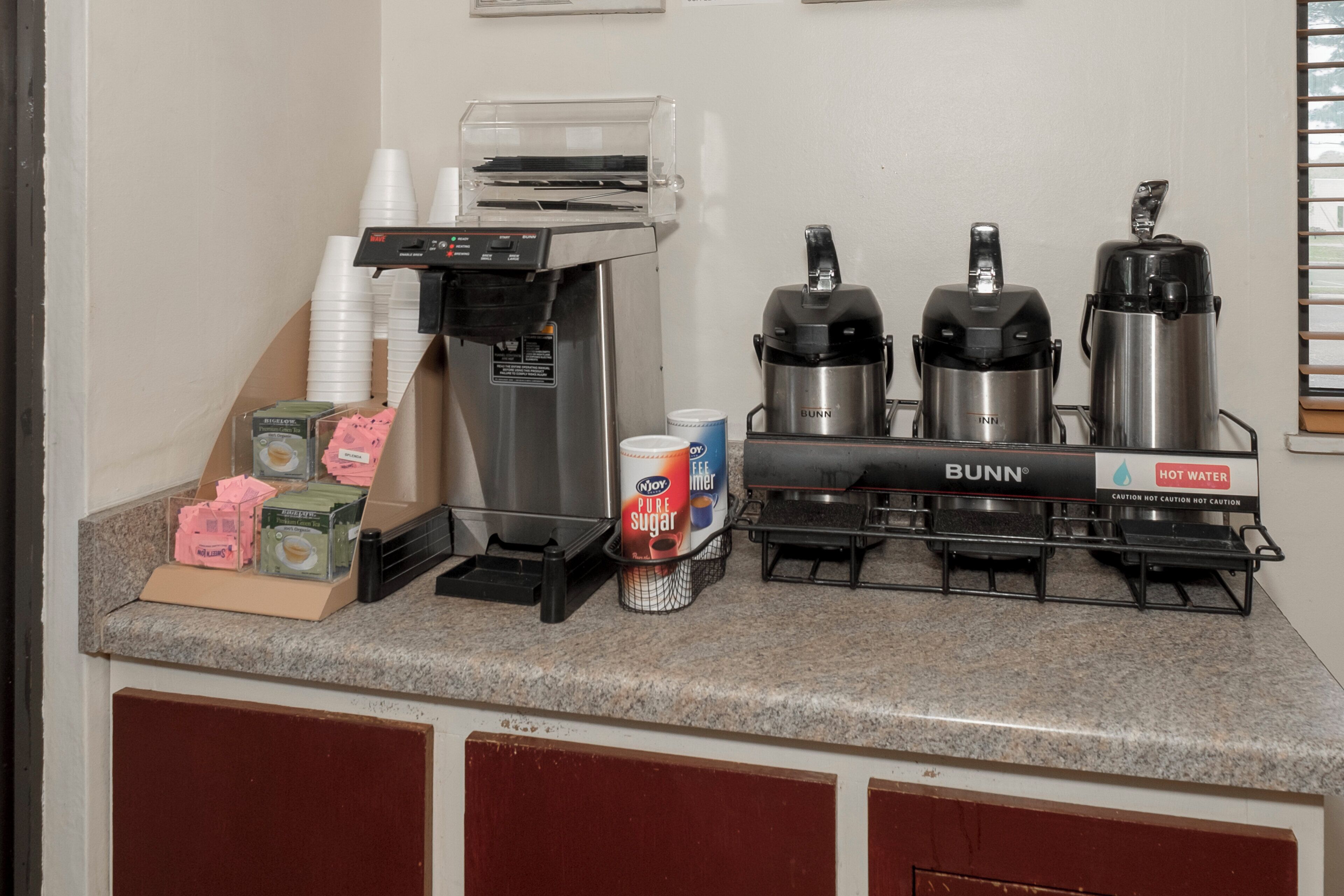 Una estación de café con una máquina de café, un dispensador de agua caliente y una jarra de café.