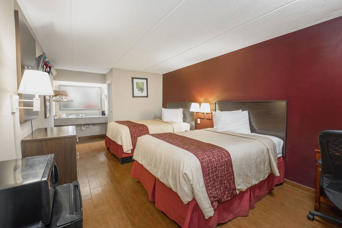 A hotel room with two beds, a desk, a mirror, and a small kitchenette.