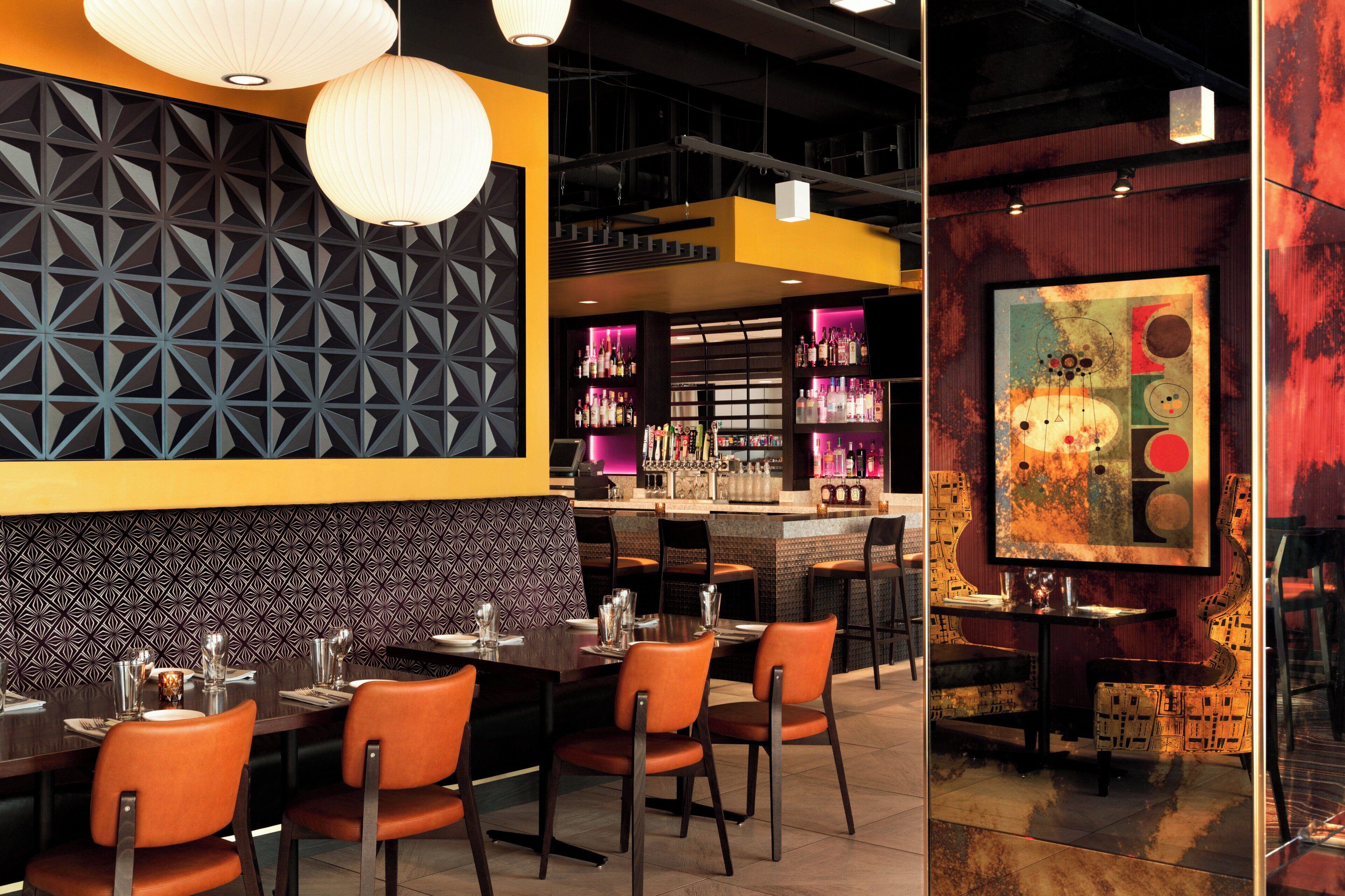 A restaurant interior with a bar area, seating with orange chairs, and a patterned wall.