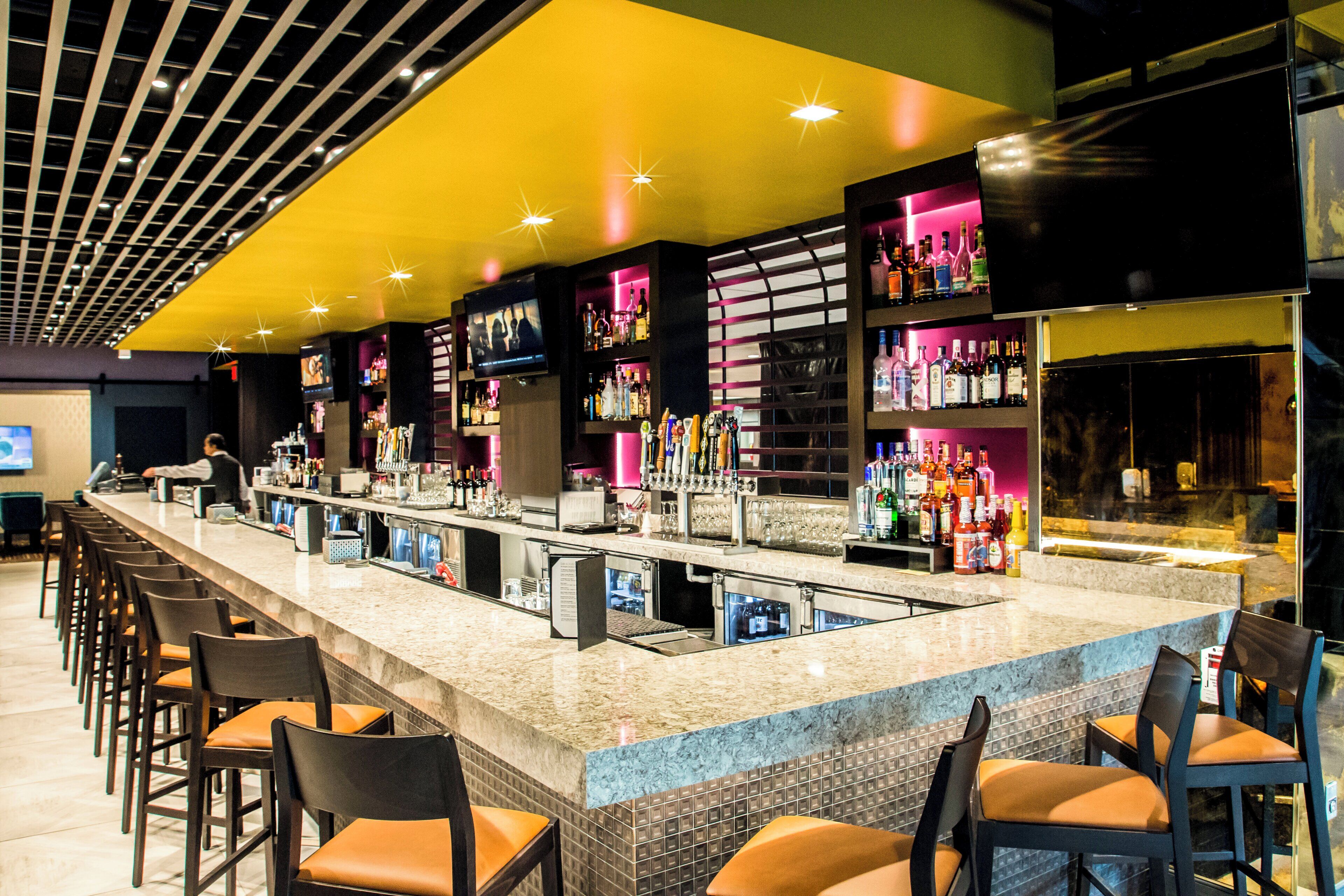 Een bar met een lange toonbank, verschillende barkrukken en een ruim assortiment flessen en glazen.