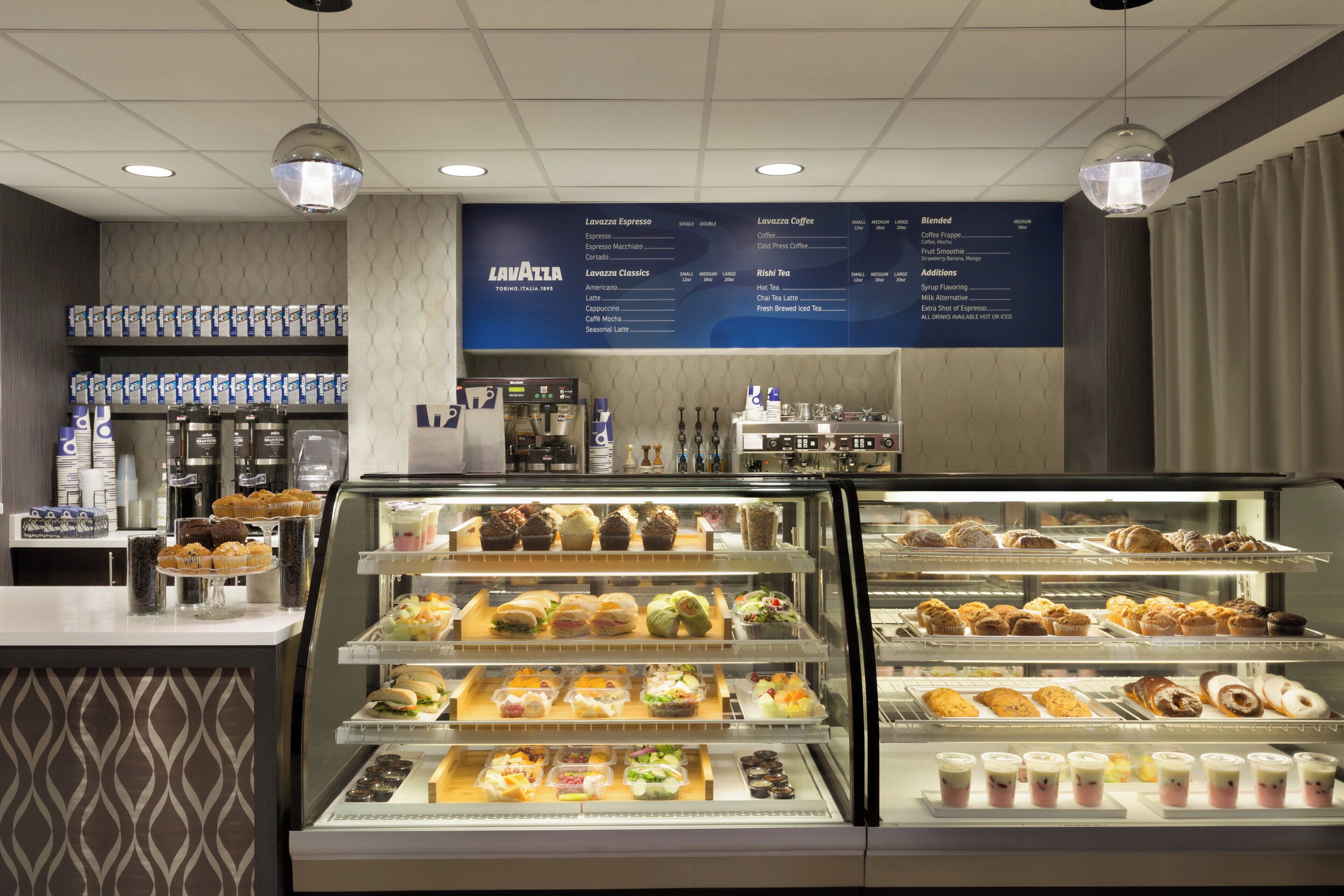 A coffee shop interior with a menu board, espresso machines, and a display case with pastries and sandwiches.