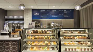 A coffee shop interior with a menu board, espresso machines, and a display case with pastries and sandwiches.
